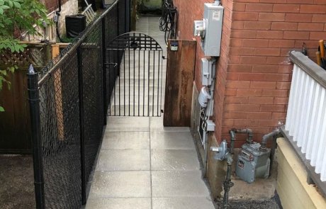 New side walkway along small side yard with security gate and black metal chain link fence